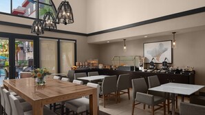 Un restaurante moderno con una mesa de comedor de madera, sillas grises y una zona de bar con electrodomésticos de cocina.