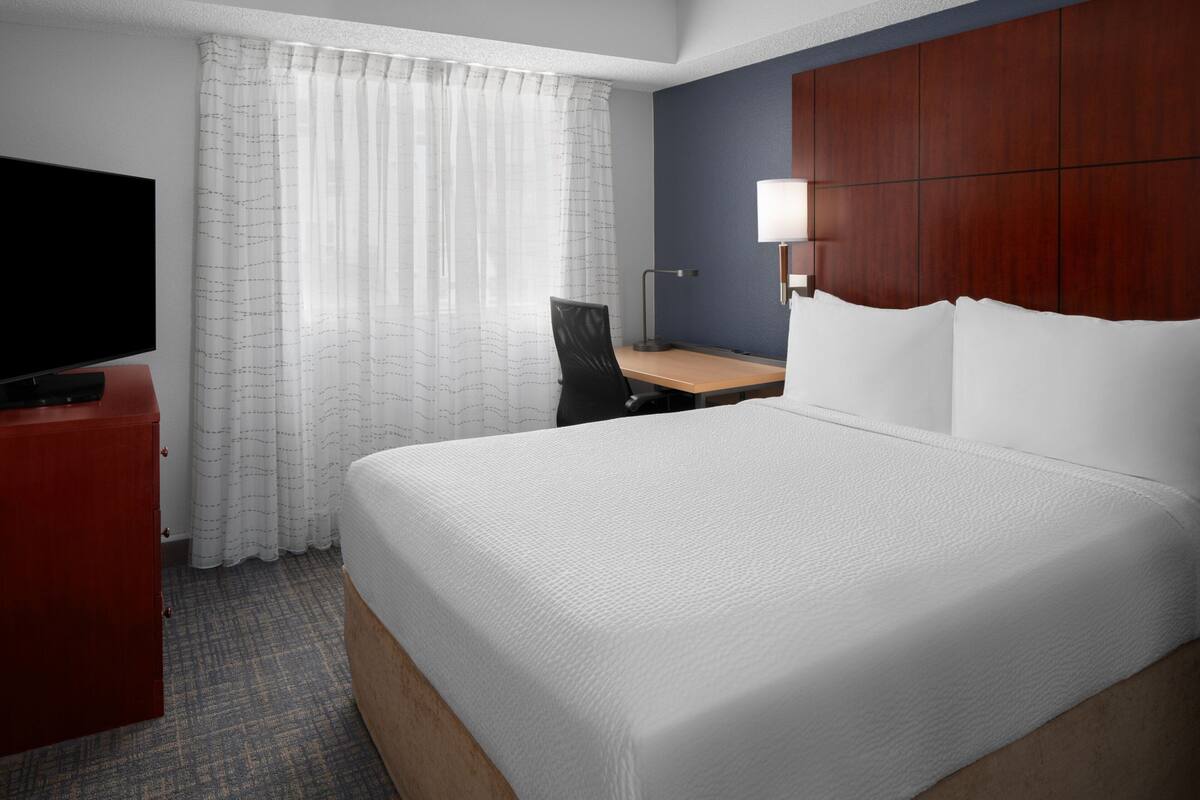 Een hotelkamer met een groot bed, een bureau, een stoel, een televisie en een raam met gordijnen.