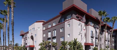 A multi-story hotel with a red and grey facade, numbered 1747, featuring balconies and a parking lot with palm trees.