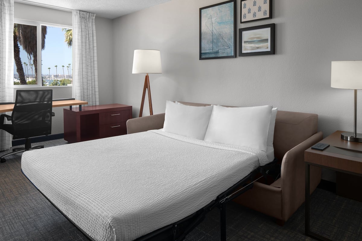 Een hotelkamer met een groot bed, een bureau, een stoel en een raam met gordijnen.