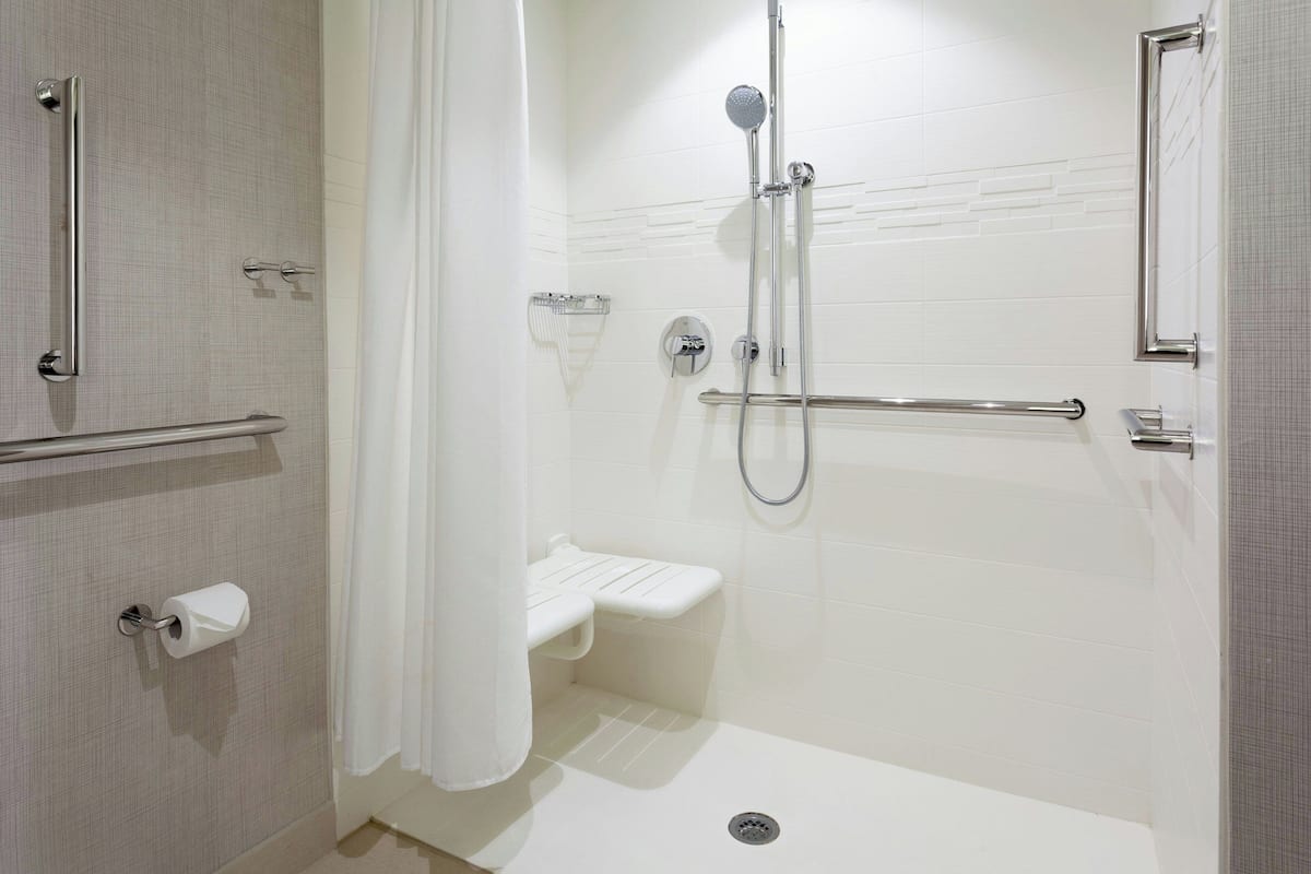 A modern bathroom with a shower, grab bars, a toilet paper holder, and a small shelf.