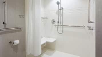 Un baño moderno con ducha, barras de apoyo, un dispensador de papel higiénico y un estante pequeño.