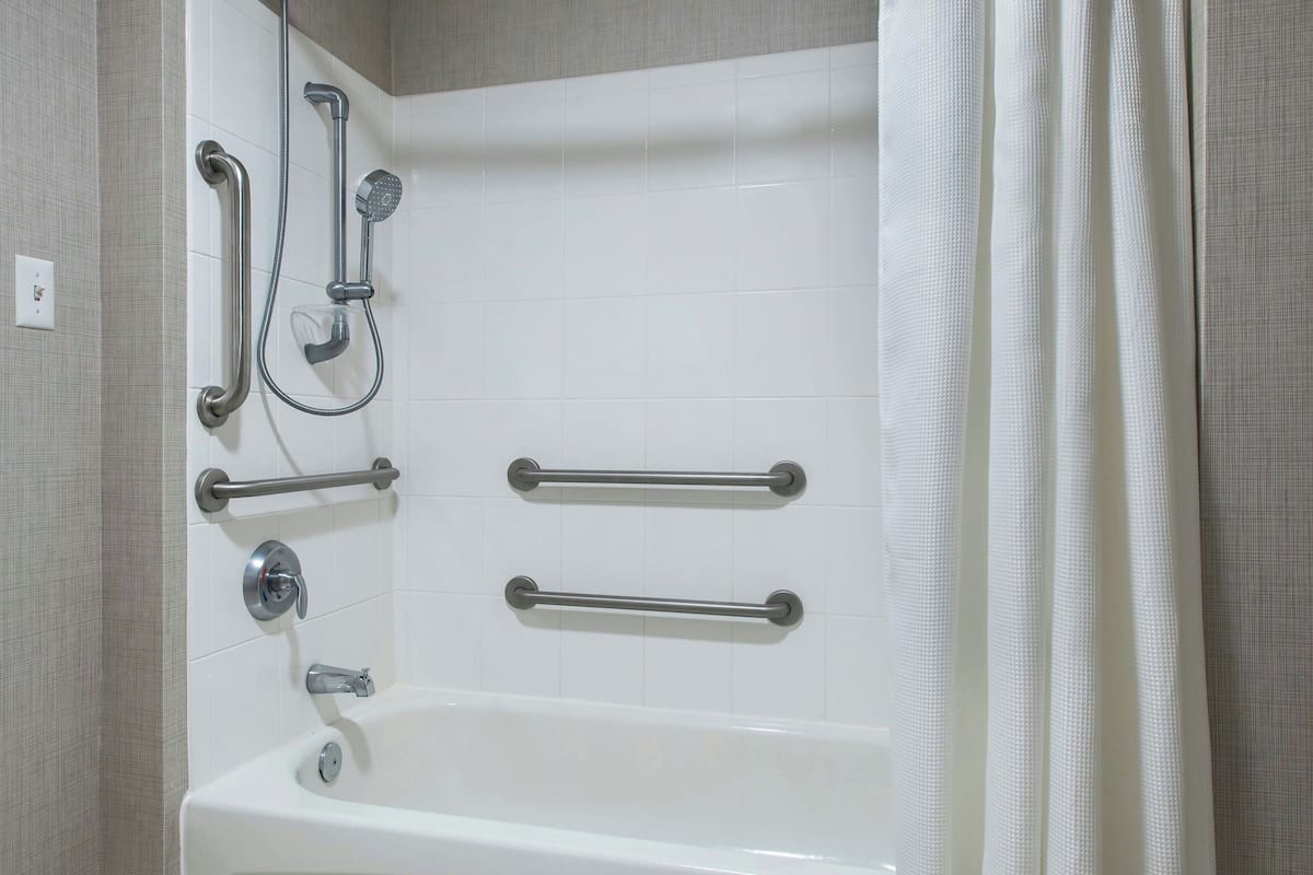 A bathroom with a white bathtub, grab bars, a showerhead, and a faucet.
