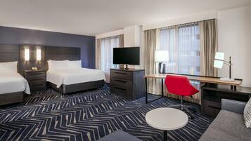 A hotel room with two beds, a desk with a TV, a red chair, and a small round table.