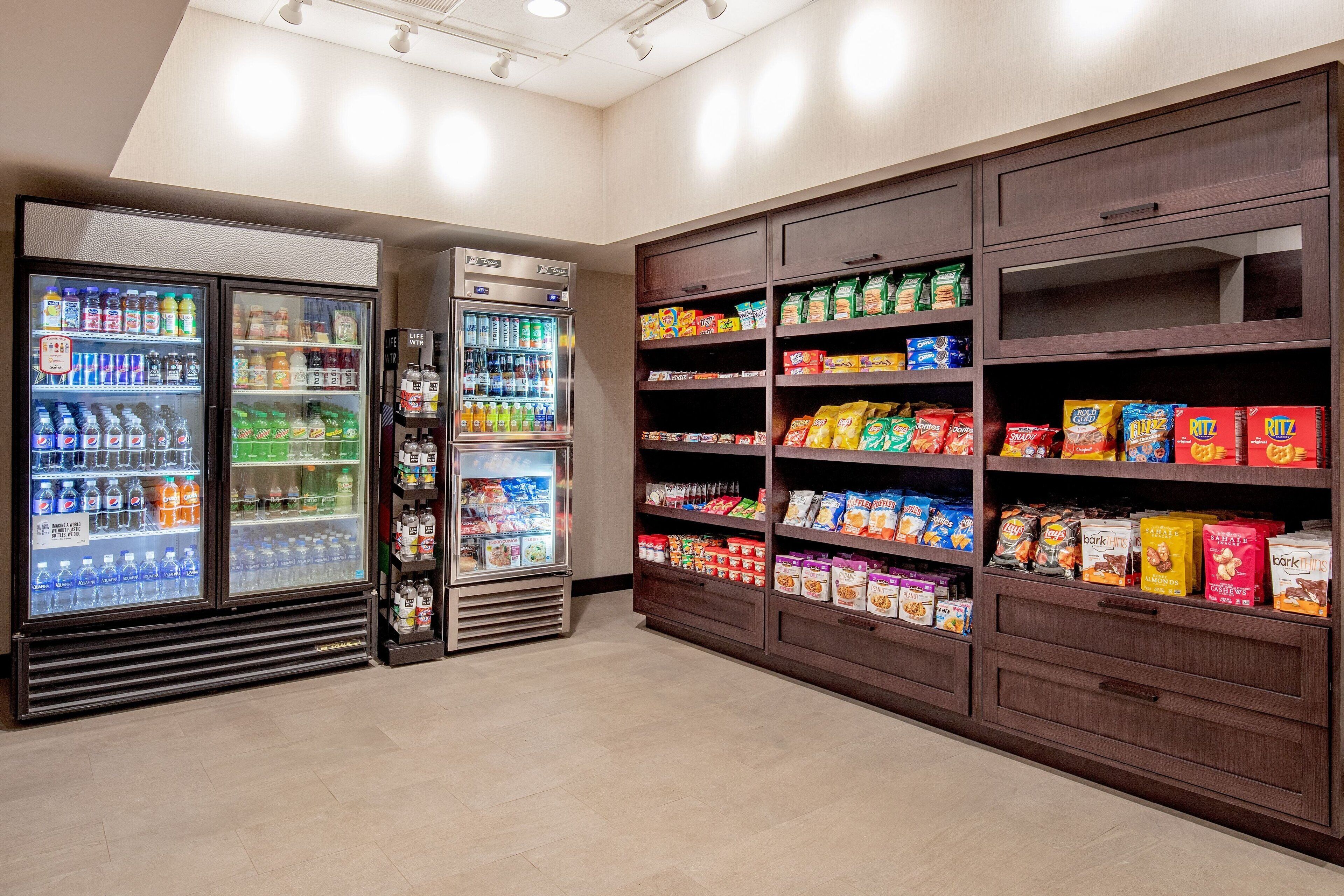 Een goed verlichte ruimte met snacks en drankjes, inclusief gekoelde drankdispensers en schappen vol met diverse snacks en verpakte producten.