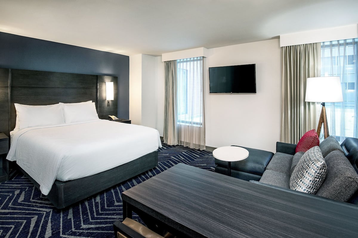 A hotel room with a large bed, a sofa, a small table, a TV, and a window with curtains.