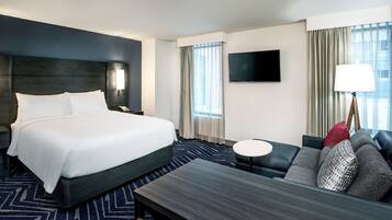 Ein Hotelzimmer mit einem großen Bett, einer Couch, einem kleinen Tisch, einem Fernseher und einem Fenster mit Vorhängen.