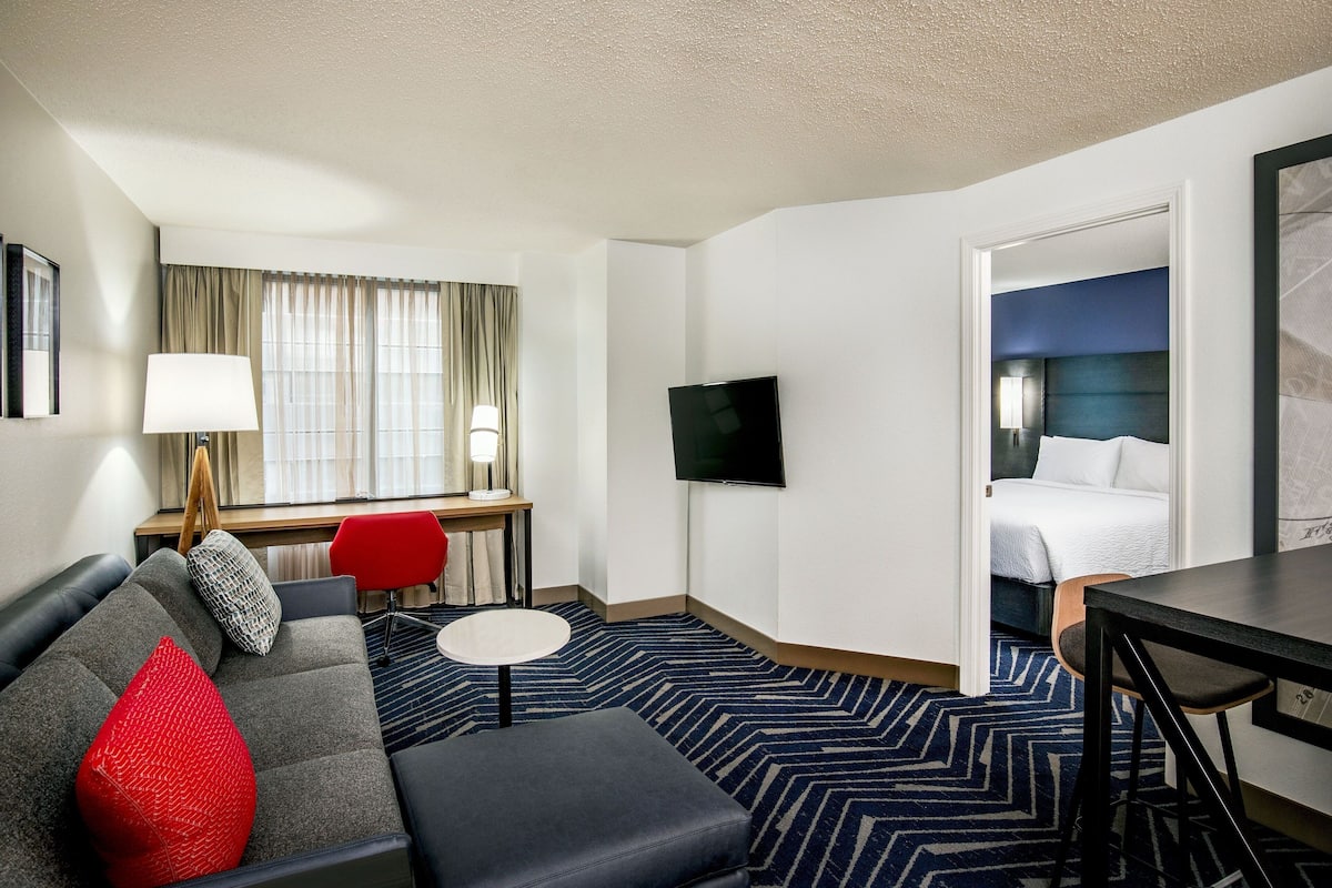 A hotel room with a sofa, a desk with a lamp, a television, a bed, and a small table.