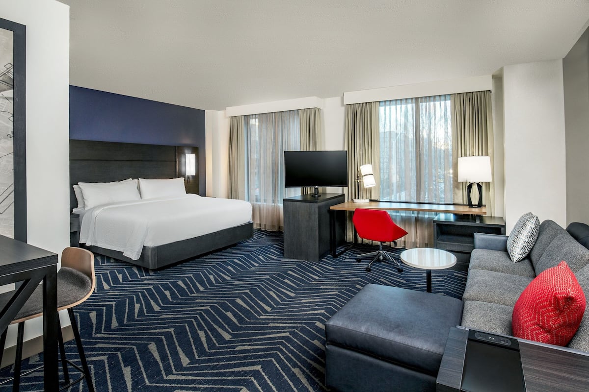 A hotel room with a bed, a desk with a TV, a sofa, and a chair.