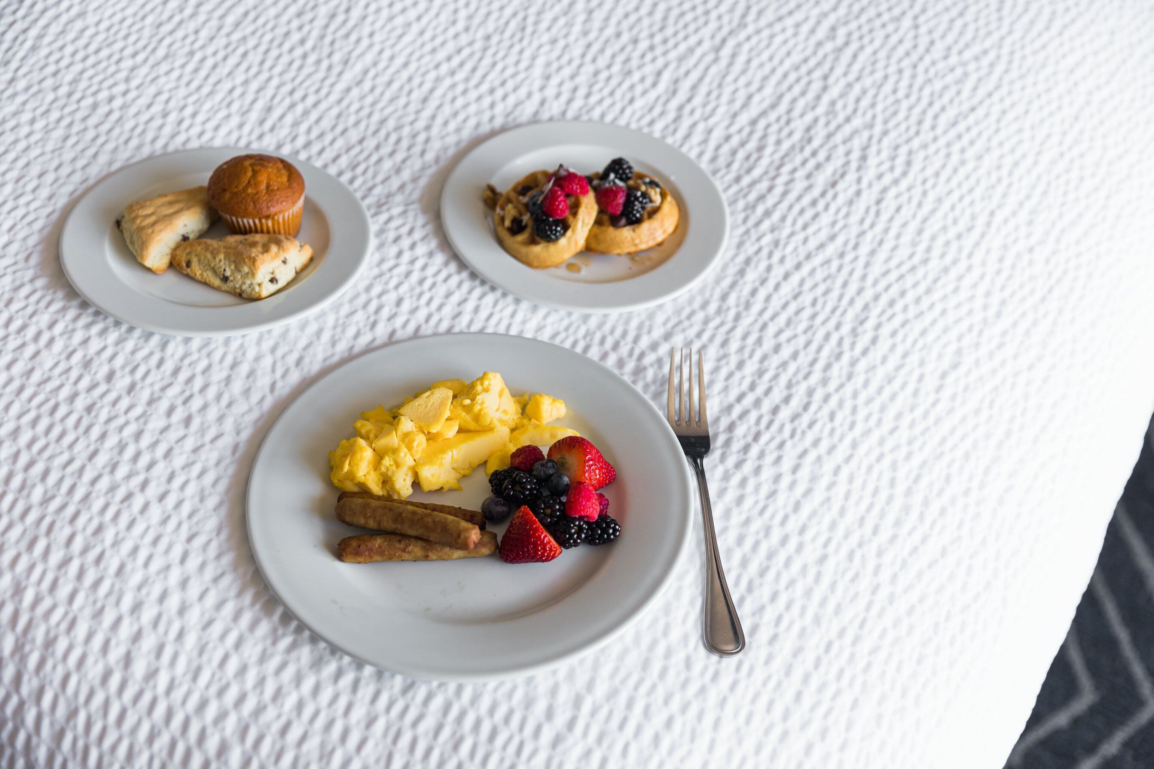 Three plates of breakfast food on a textured white tablecloth.