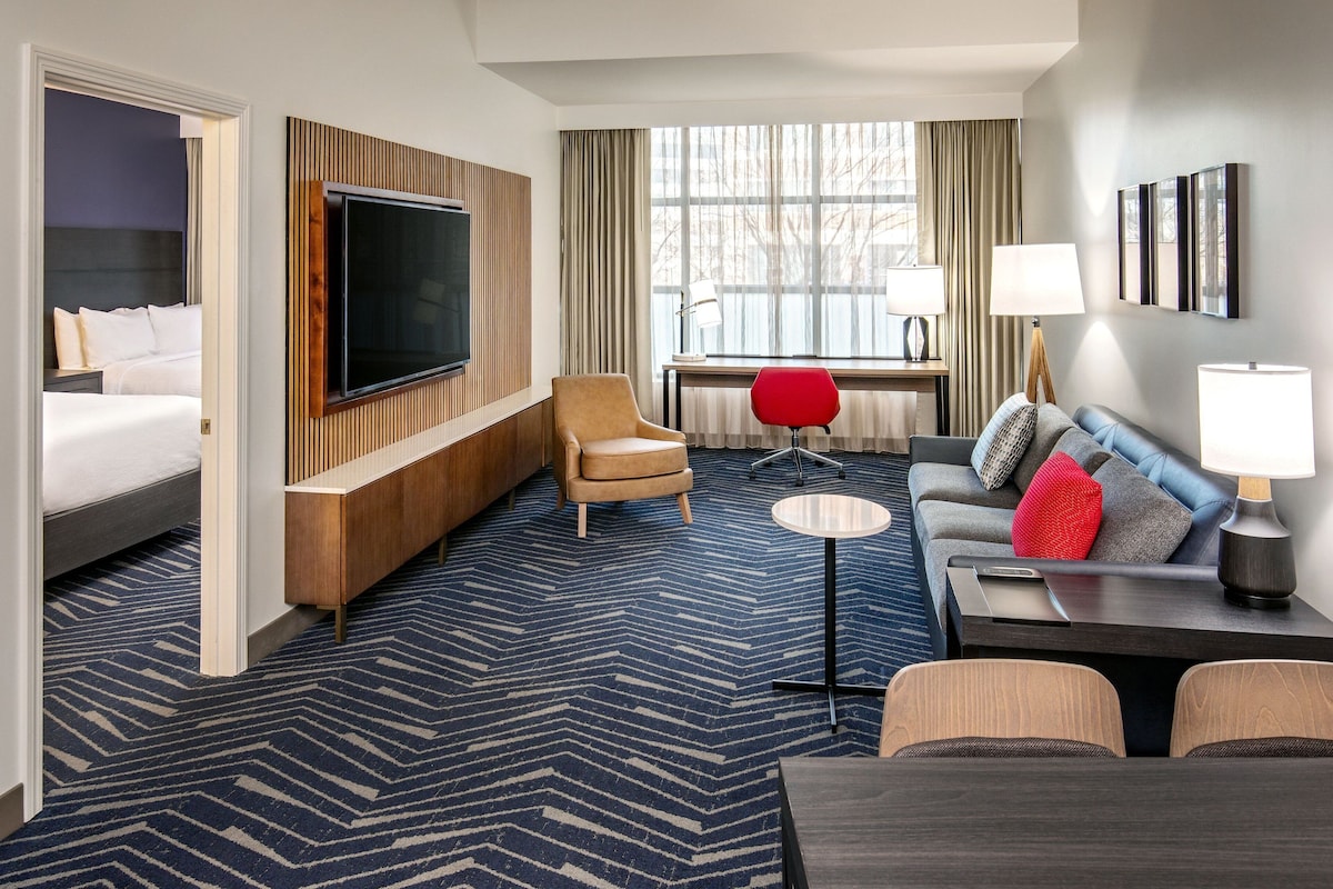 A hotel room with a bed, a TV, a sofa, a desk, and a chair.