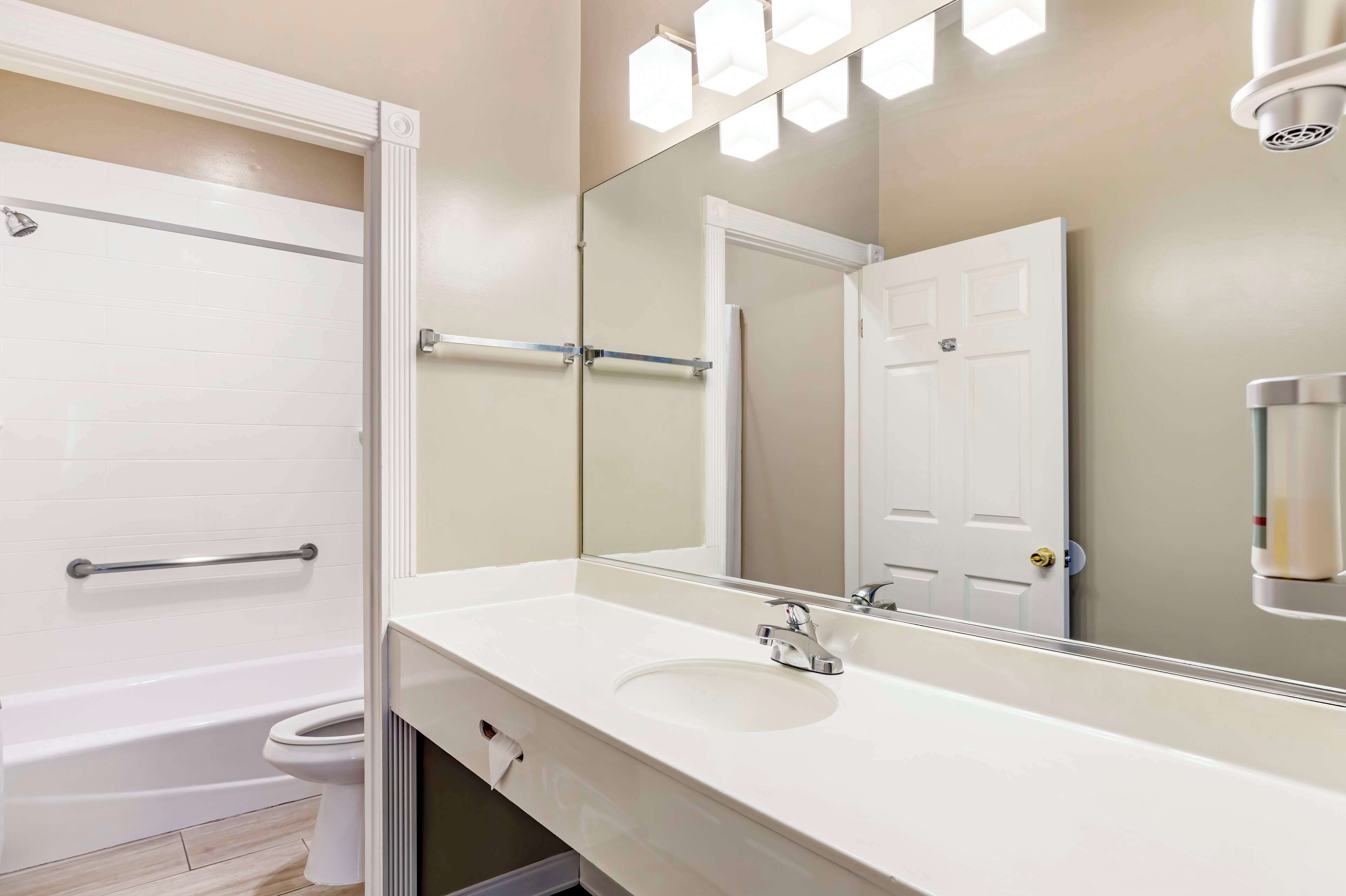 A bathroom with a white bathtub, a sink with a mirror above it, and a door with a towel rack.