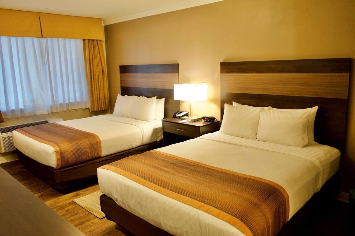 Two double beds with headboards, bedside tables, a lamp, and a window with curtains.