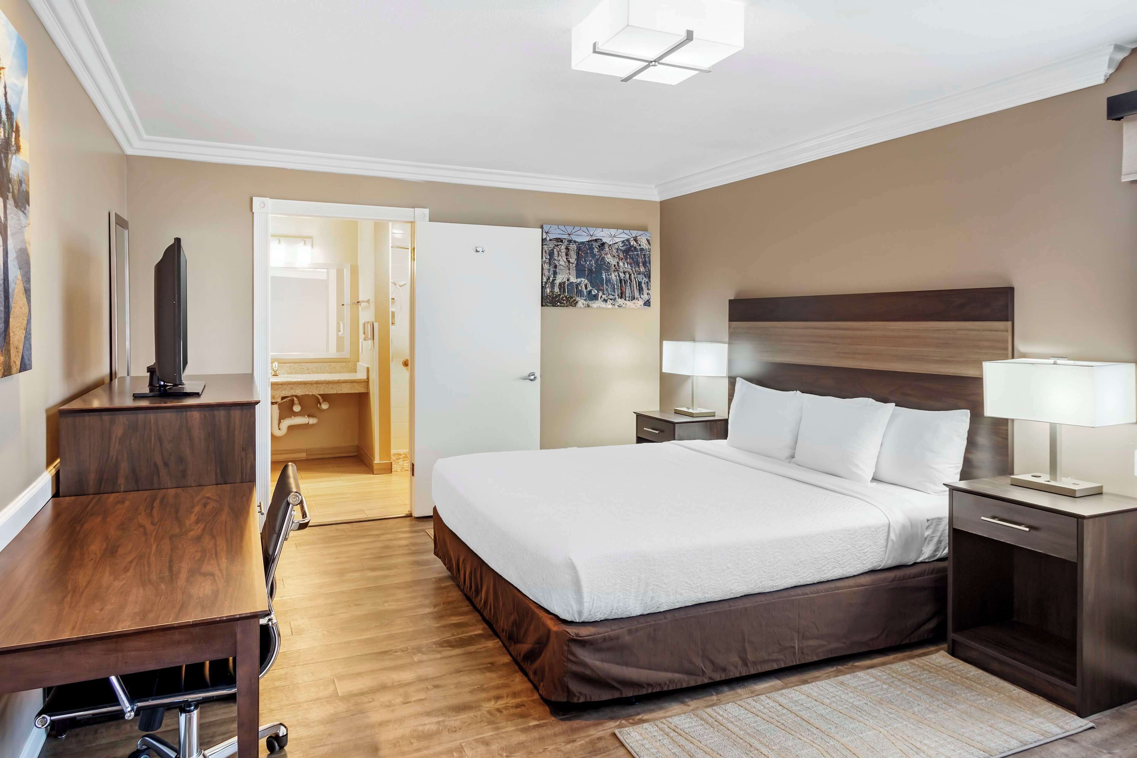 A hotel room with a large bed, bedside tables with lamps, a desk, and a television.