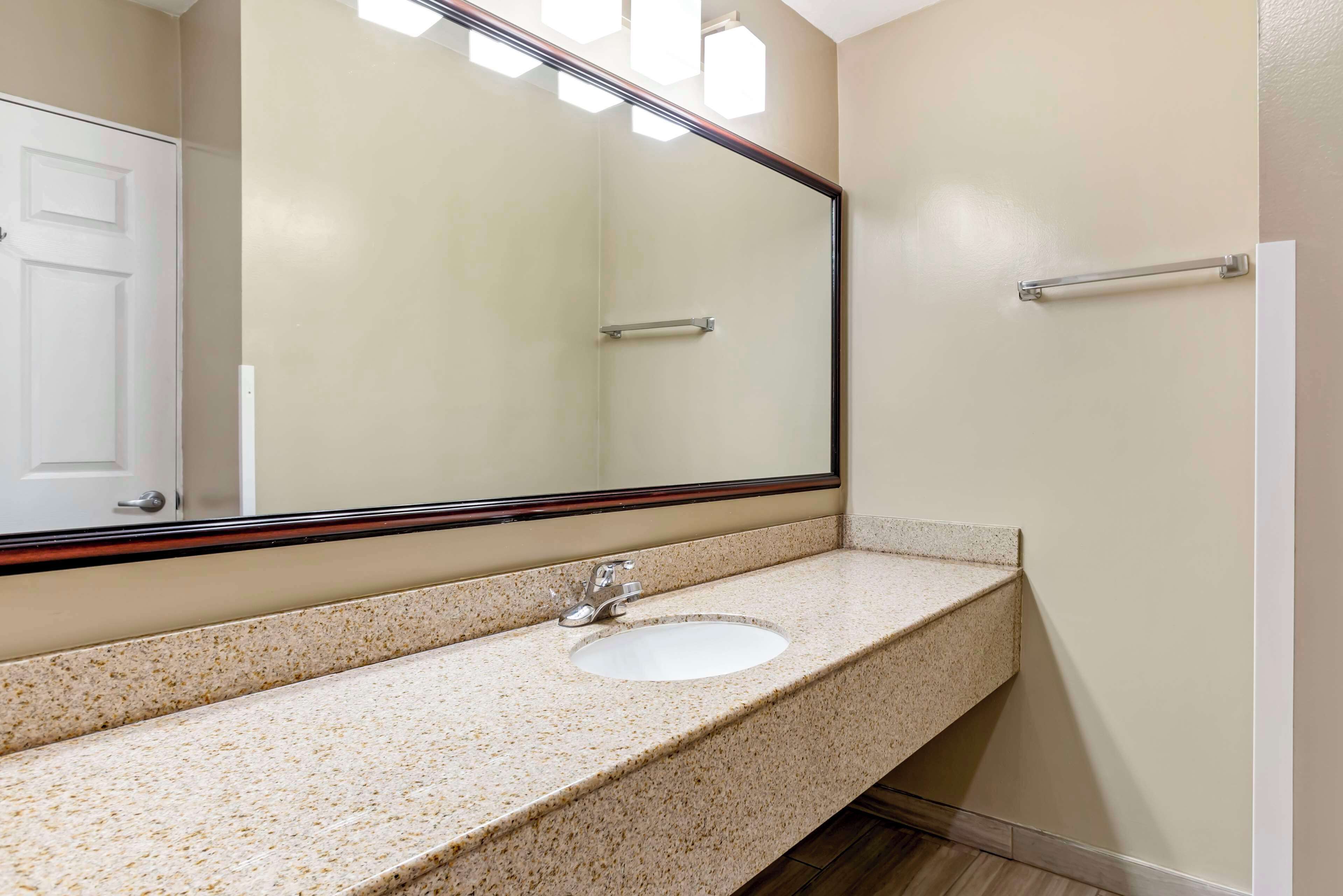 A bathroom with a granite countertop, a white sink, and a large mirror.