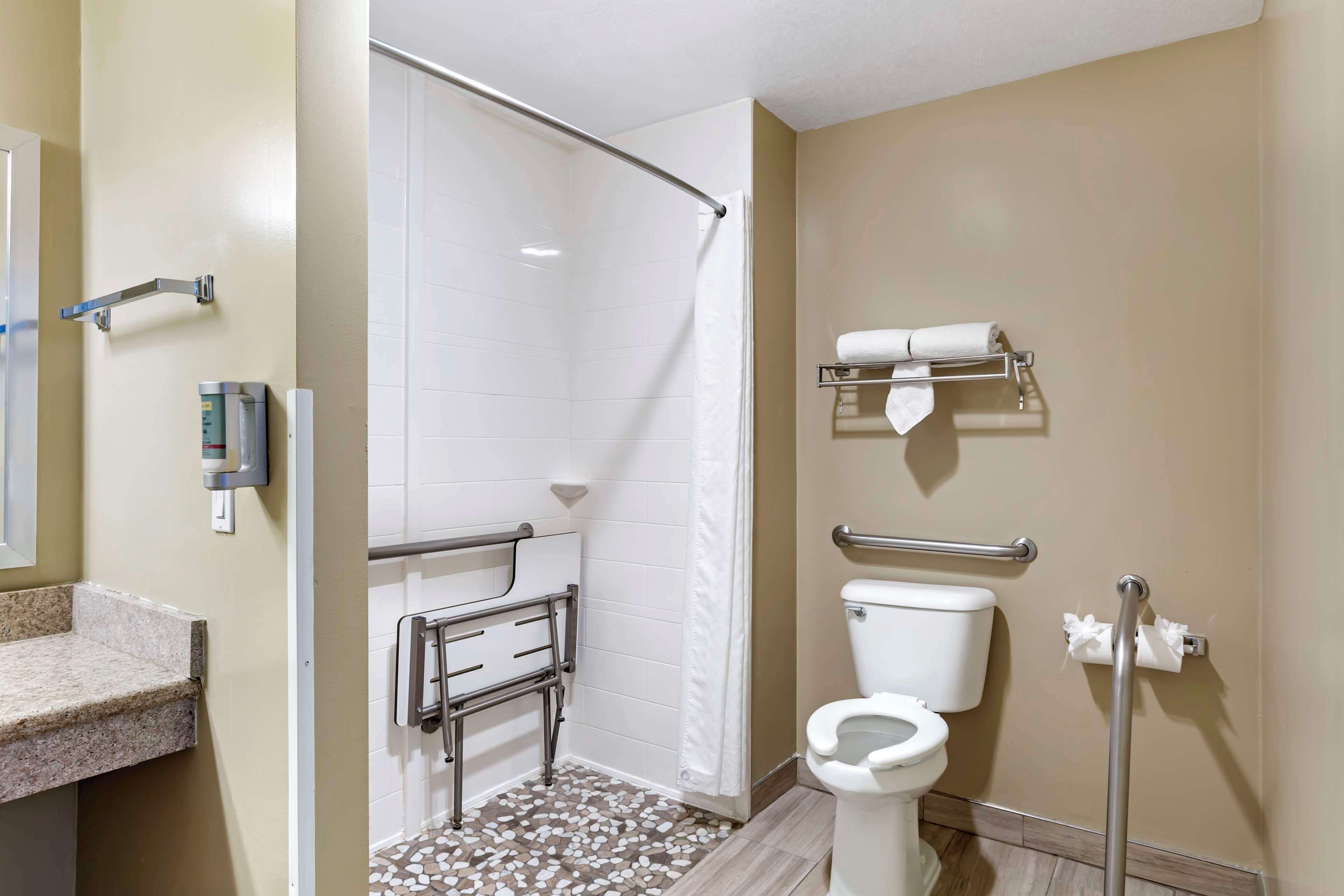 A bathroom with a shower, toilet, grab bars, and a towel rack.