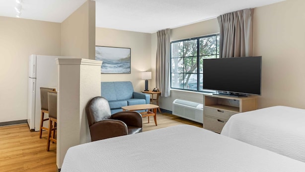 Ein Hotelzimmer mit Bett, Schreibtisch, Stuhl, Fernseher und einem Fenster mit Vorhängen.