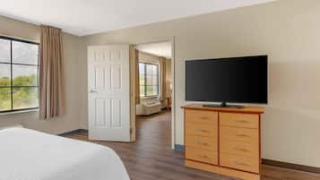 Una habitación de hotel con una cama, un televisor sobre un aparador de madera, una puerta que da a otra habitación y una ventana con cortinas.