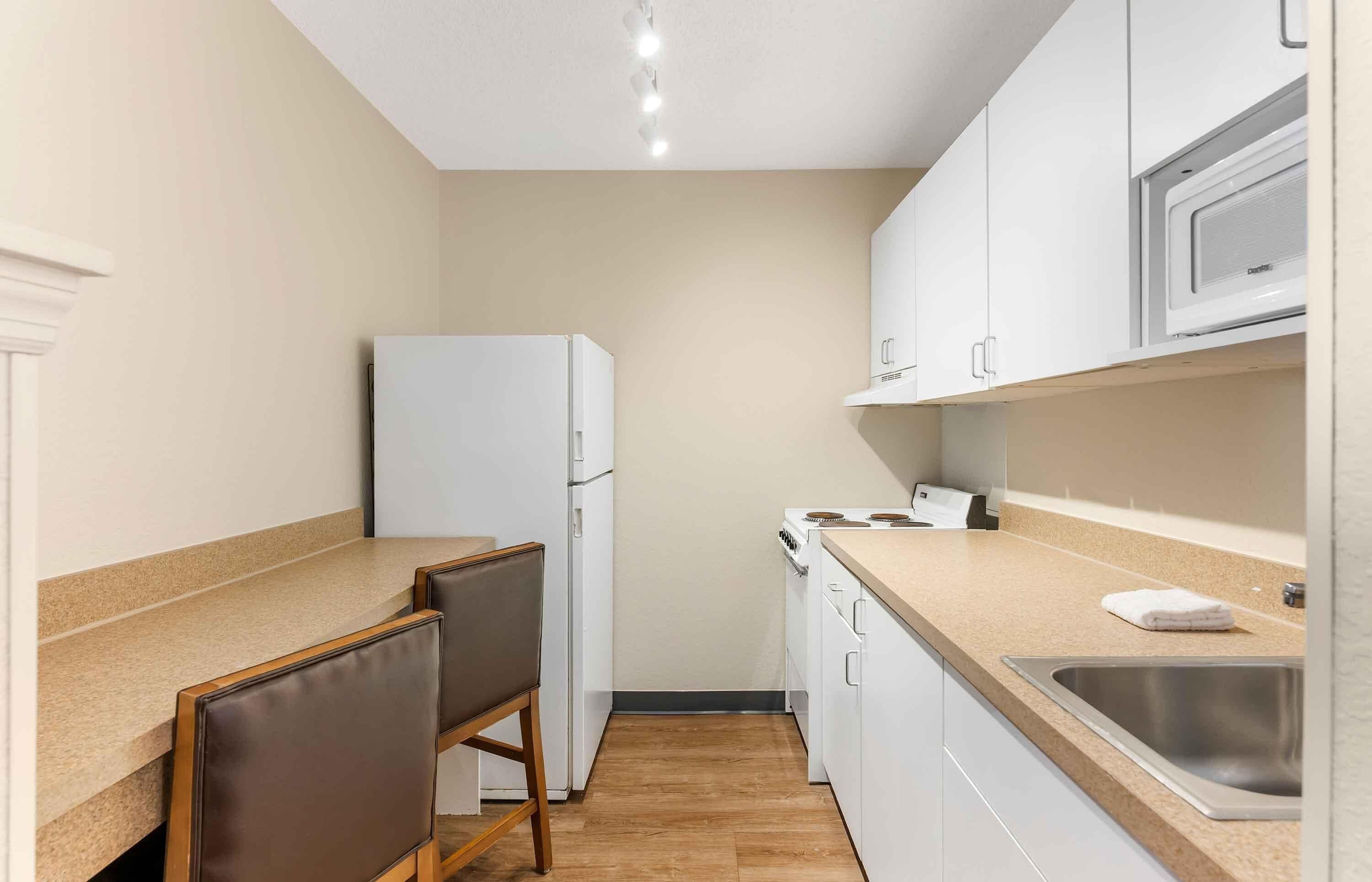 A compact kitchen with white cabinets, a built-in microwave, a sink, and a chair.