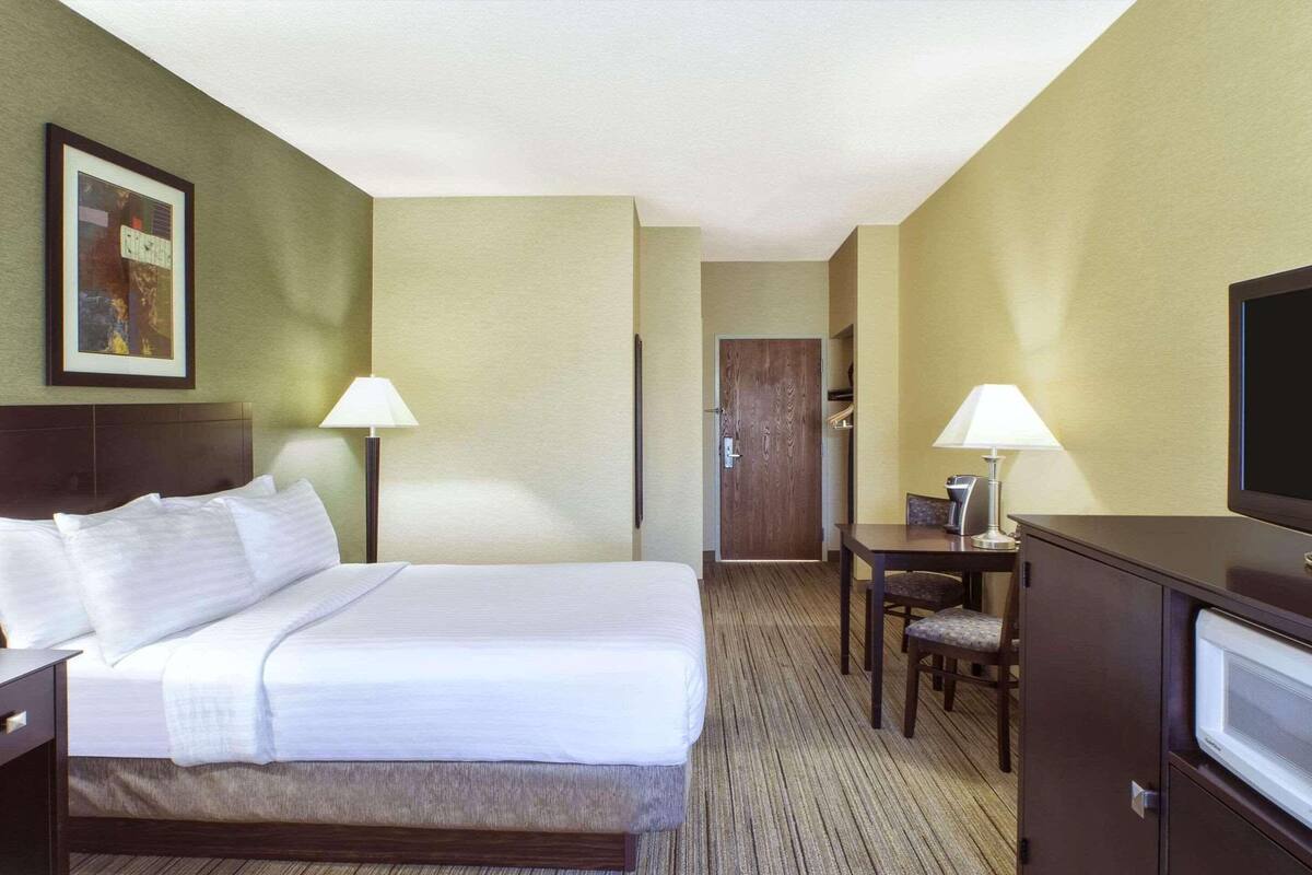 A hotel room with a bed, bedside tables, a desk with a chair, a television, and a door leading to a bathroom.