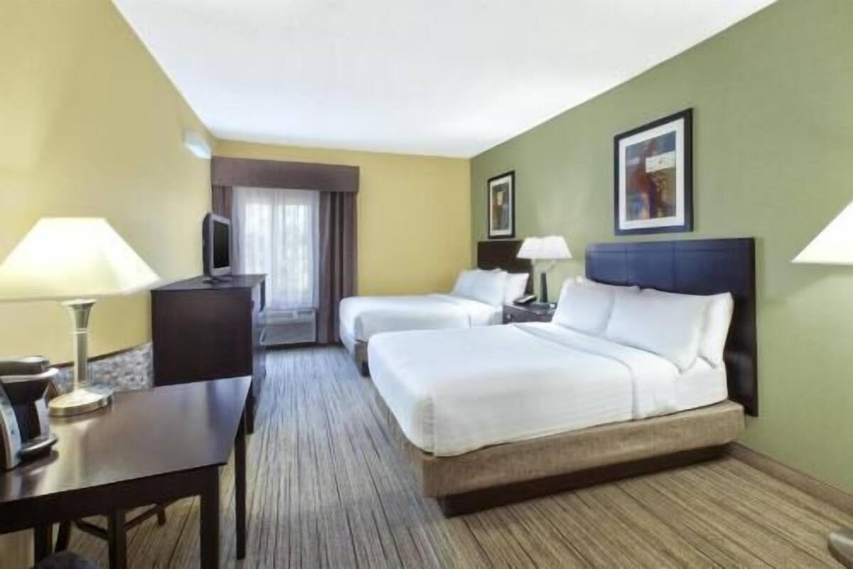 A hotel room with two beds, a desk, a TV, and a window with curtains.