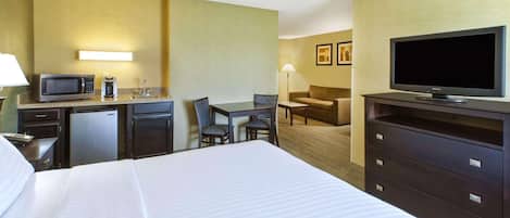 A hotel room with a bed, a desk with a computer, a television, a microwave, and a refrigerator.