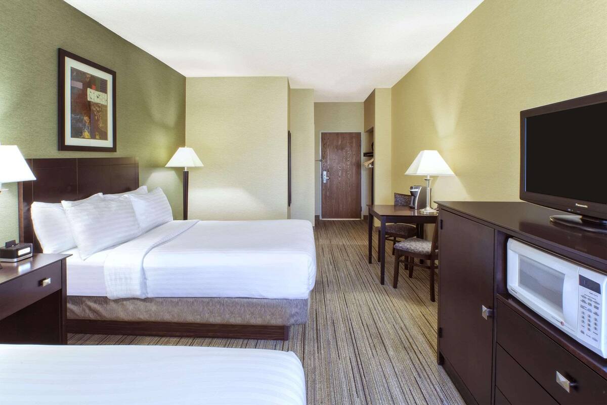 A hotel room with two beds, a desk with a chair, a television, and a microwave.