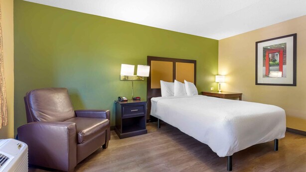 A hotel room with a bed, a chair, a nightstand, a lamp, and a framed picture on the wall. - Extended Stay America Suites Los Angeles Torrance Del Amo Ci (Torrance)