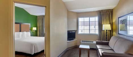 A hotel room with a bed, a TV, a sofa, and a window with curtains.