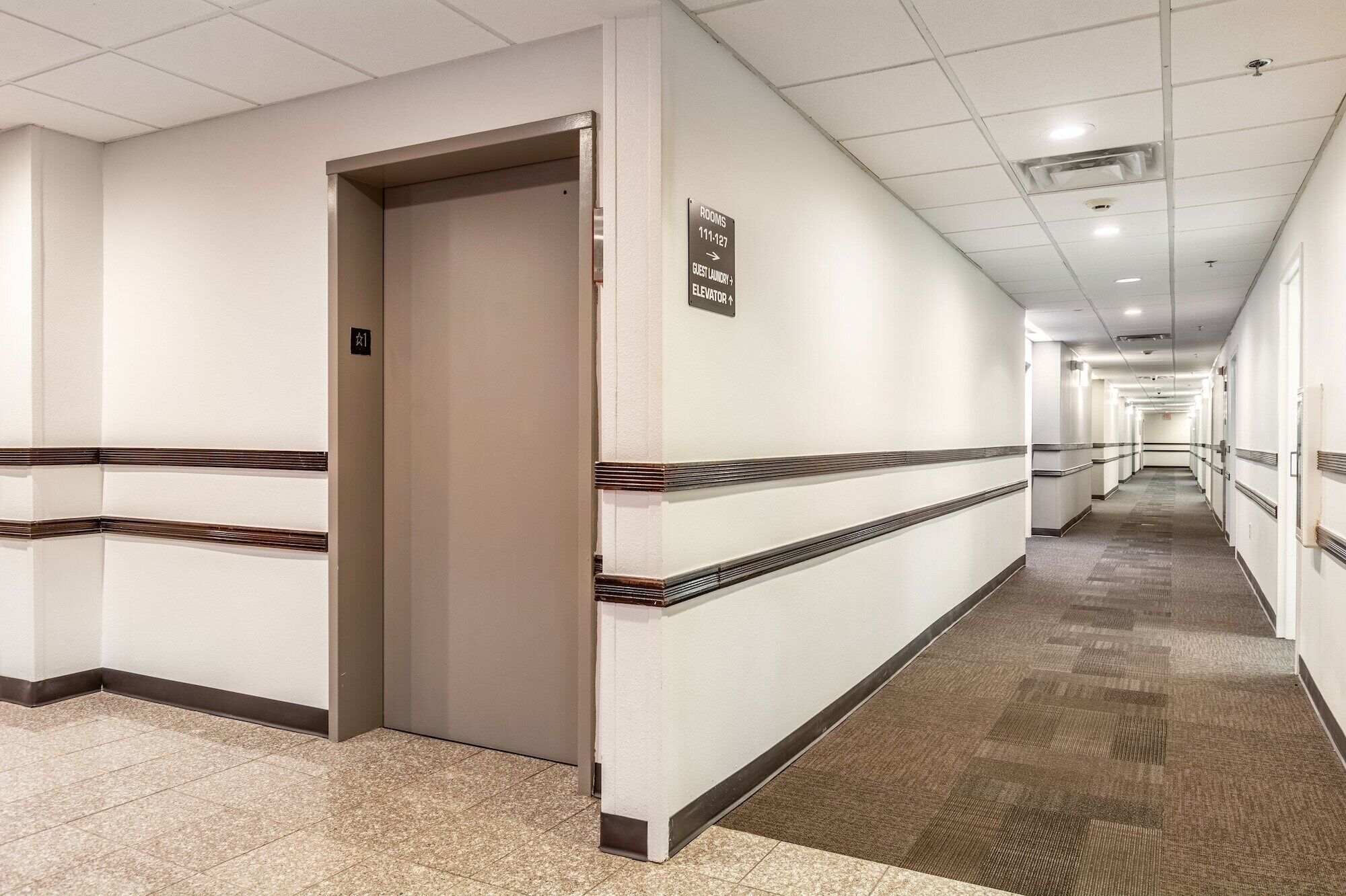 A hotel corridor with a carpeted floor, white walls, and a sign indicating rooms 111-127.
