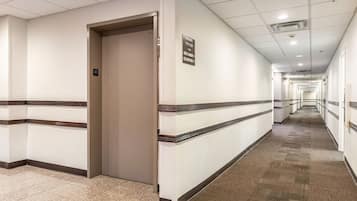 A hotel corridor with a carpeted floor, white walls, and a sign indicating rooms 111-127.