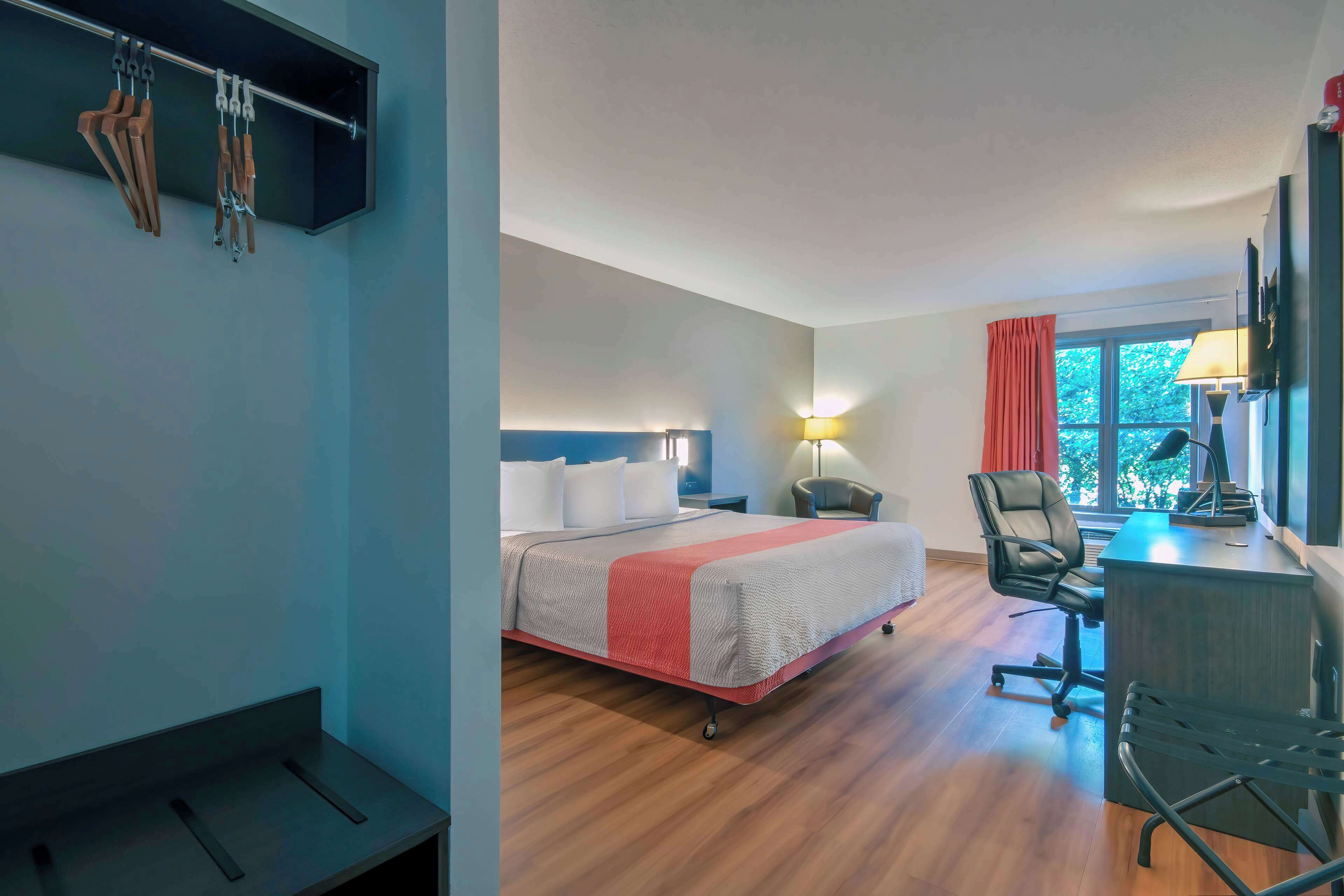 A hotel room with a bed, desk, chair, and a wall-mounted coat rack.