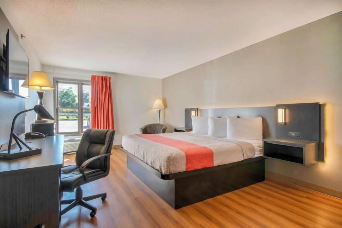Habitación de hotel con cama, escritorio, silla y vistas al exterior.