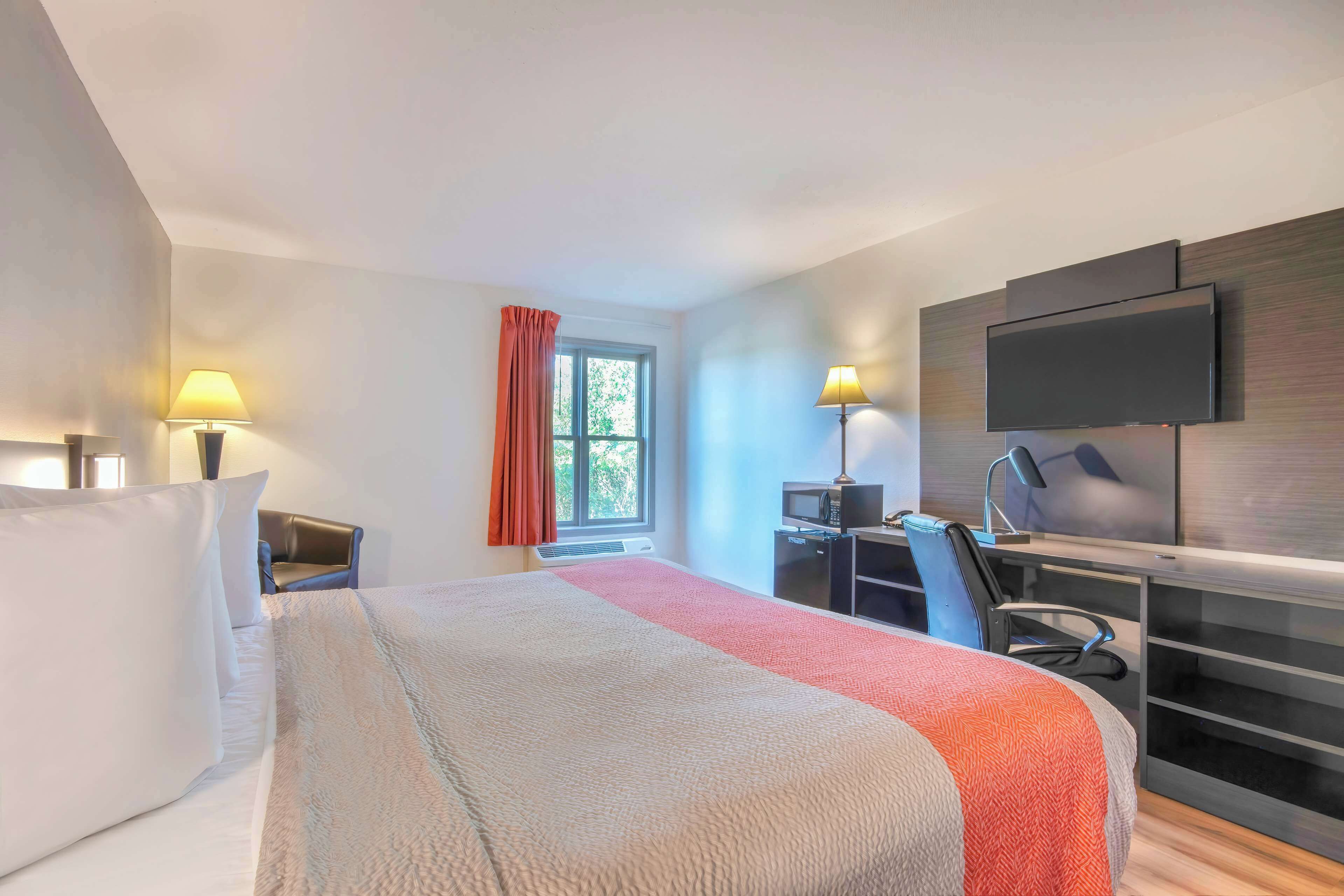A hotel room with a bed, a desk with a computer, a TV, and a window with curtains.