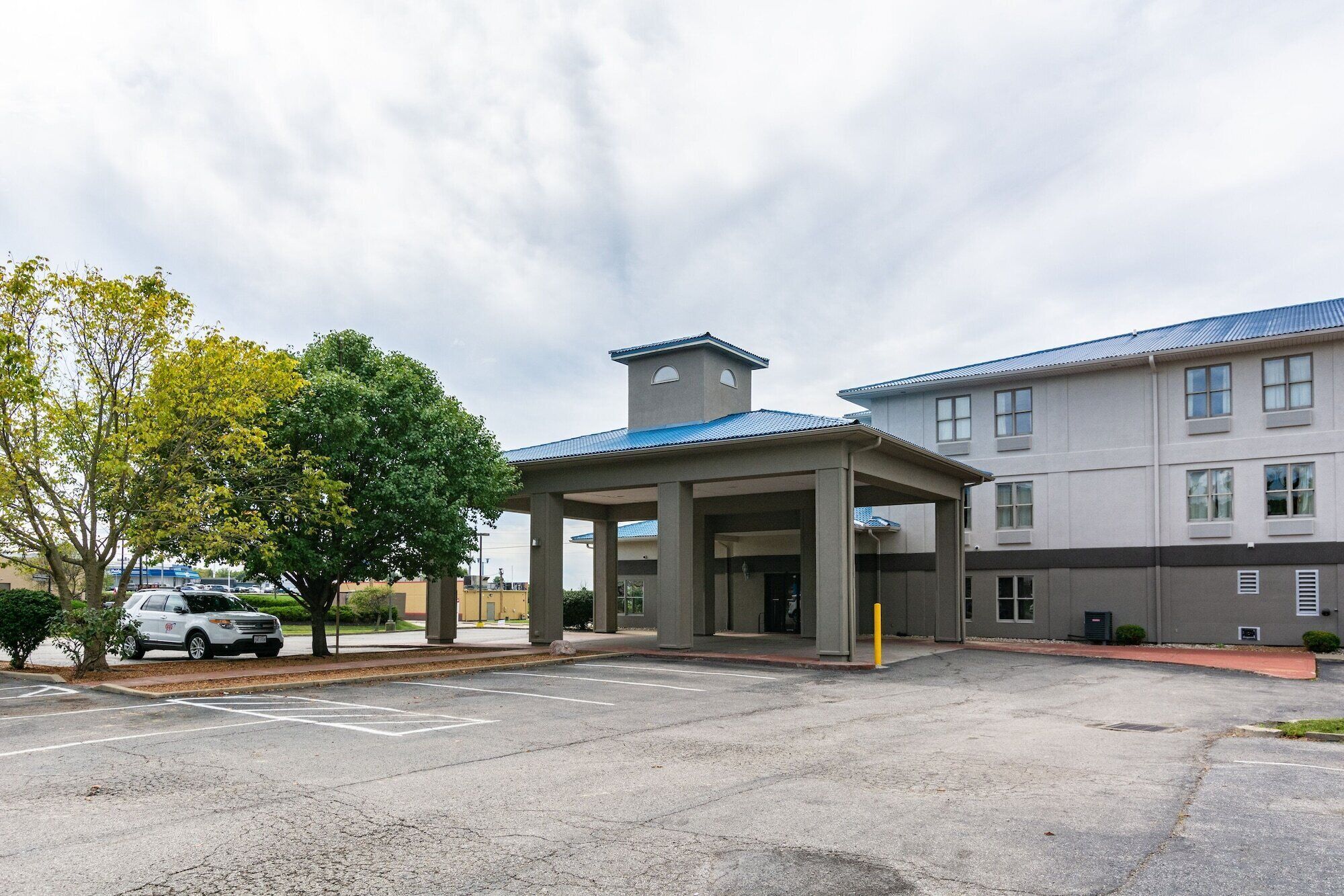 Entrada de hotel com área de espera coberta, estacionamento e edifício com telhado azul.