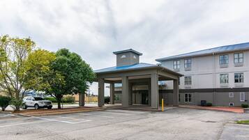 Entrada de hotel com área de espera coberta, estacionamento e edifício com telhado azul.