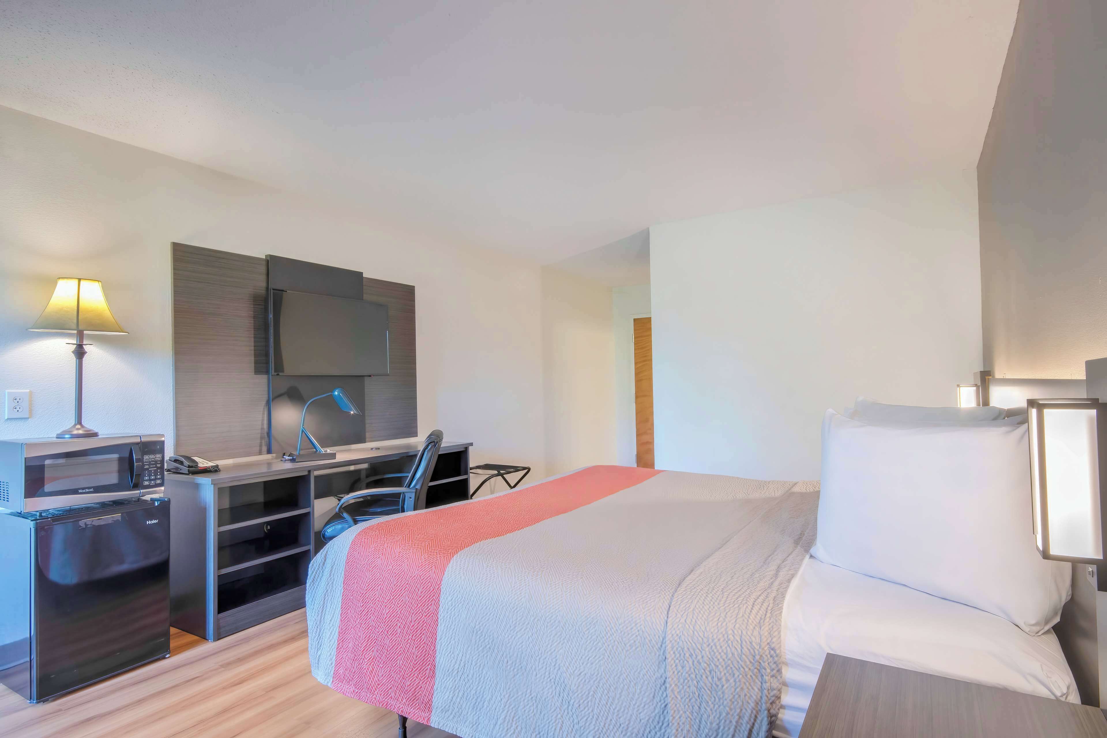 A hotel room with a bed, a desk with a computer, a microwave, and a refrigerator.