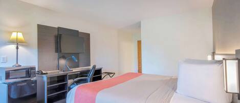 Una habitación de hotel con una cama, un escritorio con computadora, un microondas y un refrigerador.