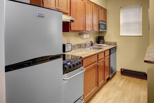 A compact kitchen with a refrigerator, stove, microwave, and wooden cabinets.