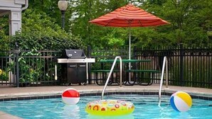 Une piscine avec des jeux gonflables et, au fond, un barbecue.