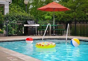 A swimming pool with inflatable toys and a barbecue grill in the background.
