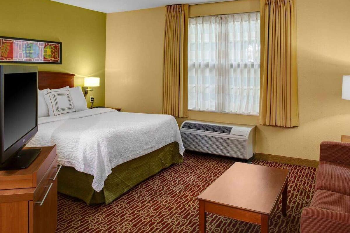 Een hotelkamer met een bed, een televisie, een bureau, een stoel en een raam met gordijnen.