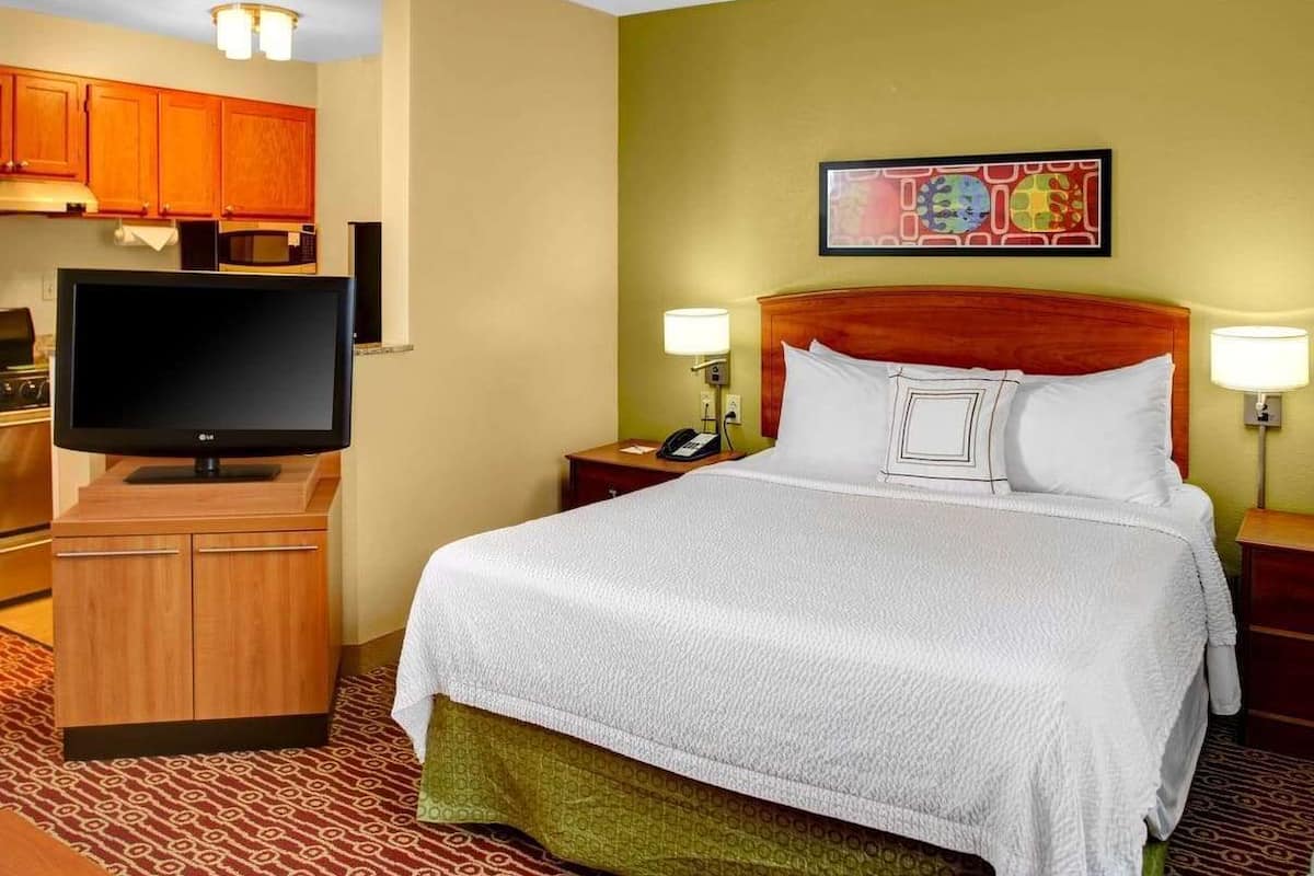 Een hotelkamer met een bed, een televisie, een magnetron en een houten kast.