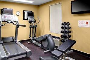 Un gimnasio con cintas de correr, elíptica, banco y estante con mancuernas.