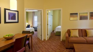 Une chambre d’hôtel comprenant une table à manger, un canapé, un lit et une salle de bain, le tout visible à travers une porte ouverte.