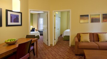 A hotel room with a dining table, a sofa, a bed, and a bathroom visible through an open door.
