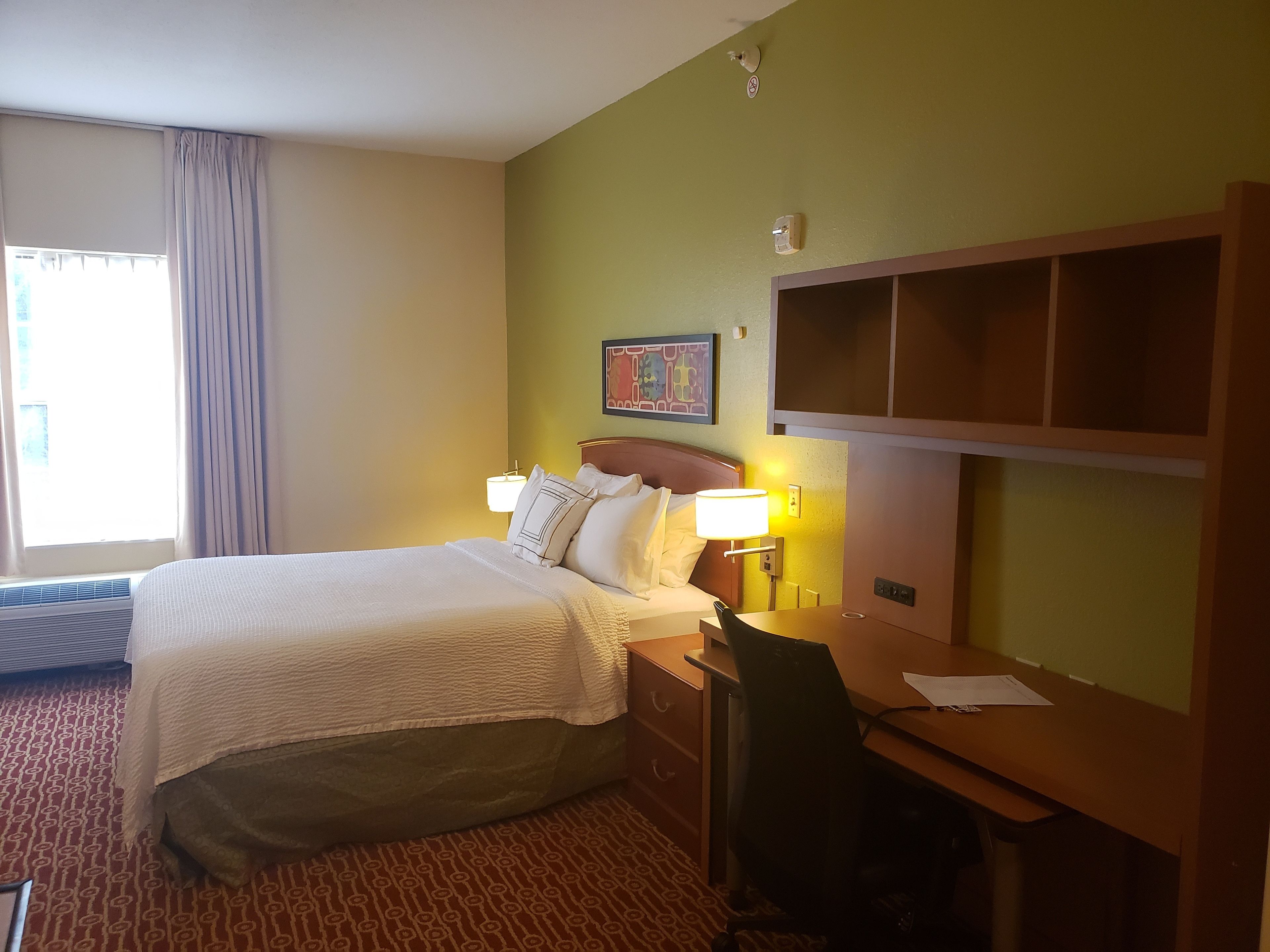 Een hotelkamer met een bed, bureau, stoel en raam met gordijnen.