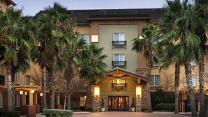 A hotel with a central entrance, multiple balconies, and surrounding palm trees.
