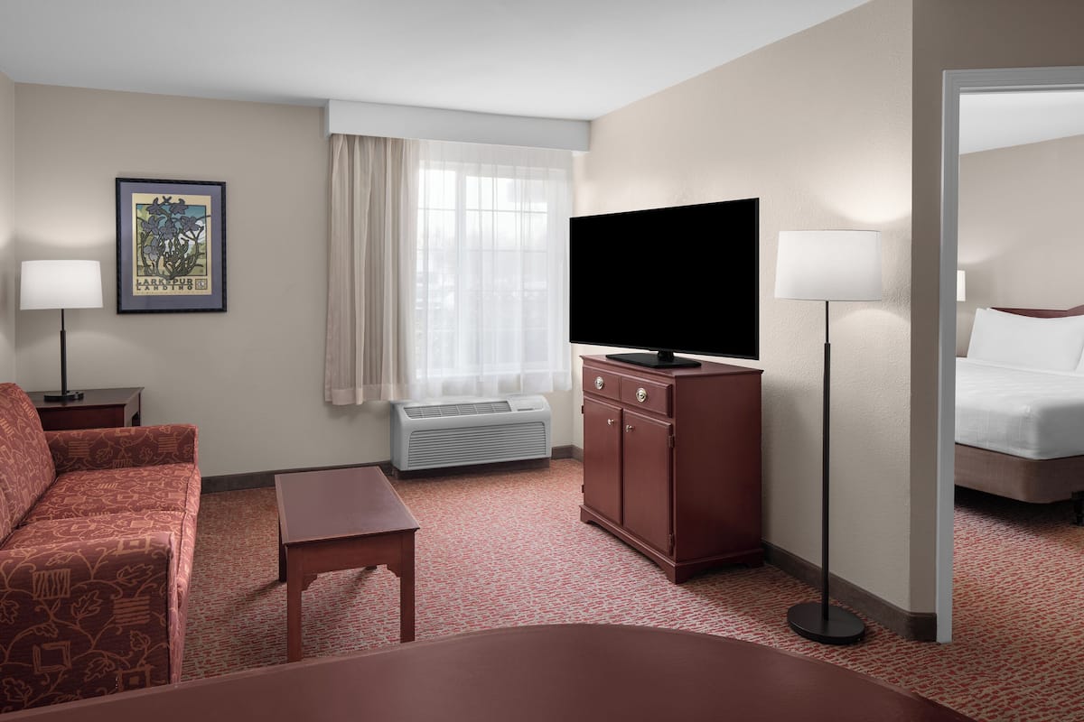 A hotel room with a bed, a TV, a desk, a chair, a dresser, and a window with curtains.