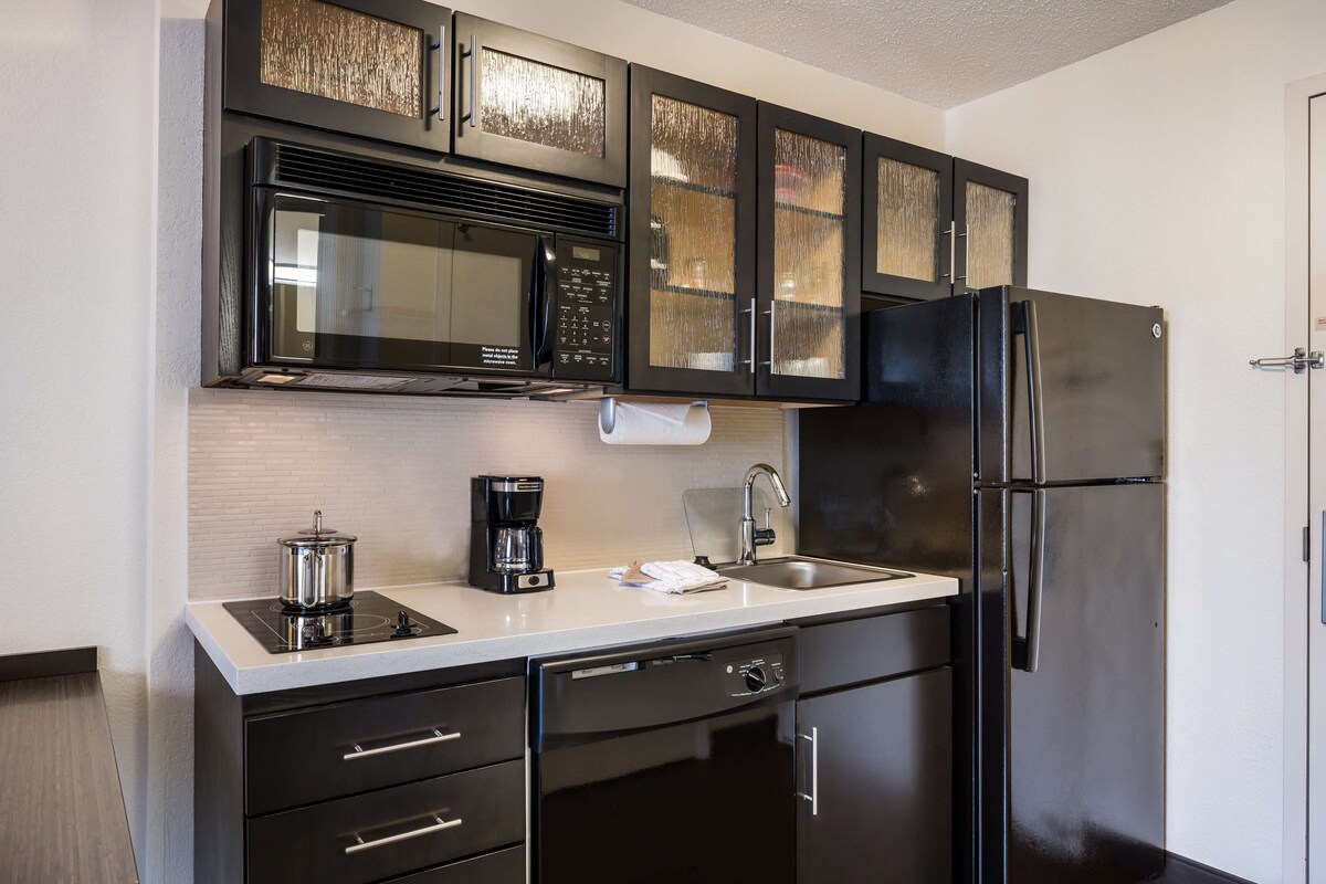 A modern kitchen with black cabinetry, a stainless steel refrigerator, a microwave, and a coffee maker.